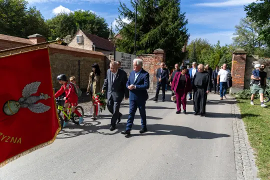 Uczestnicy uroczystości idą w procesji, niektórzy niosą kwiaty.