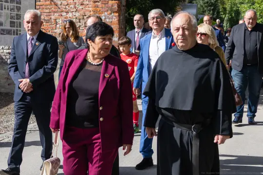 Grupa osób w formalnych strojach spaceruje po ulicy, wśród nich mężczyzna w habicie.