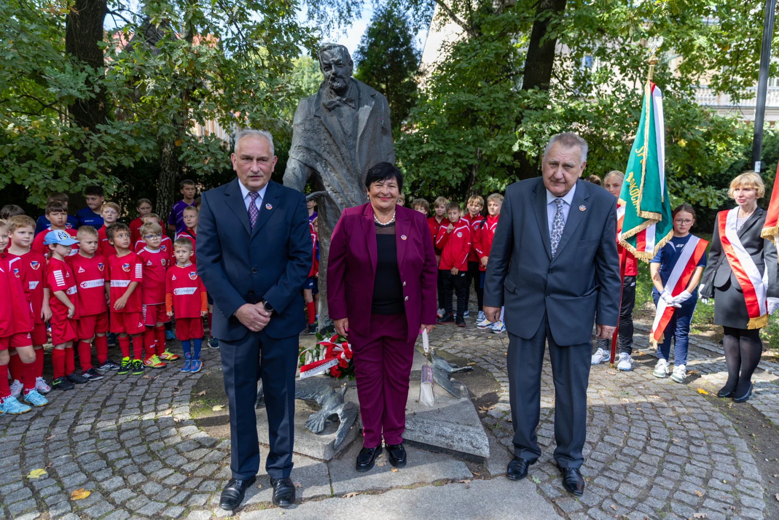 Uroczystość przy pomniku, uczestnicy w strojach galowych, dzieci w strojach piłkarskich w tle.  Autor: Bogusław Świerzowski