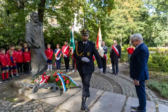 Uroczystość składania wieńców przy pomniku, obecność dzieci i przedstawicieli władz.