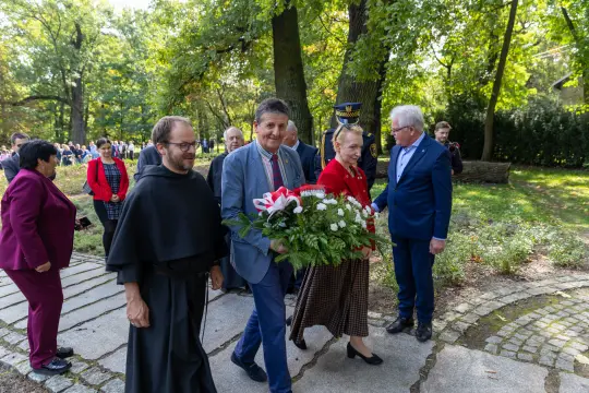Grupa ludzi w tradycyjnych strojach niesie kwiaty w parku.