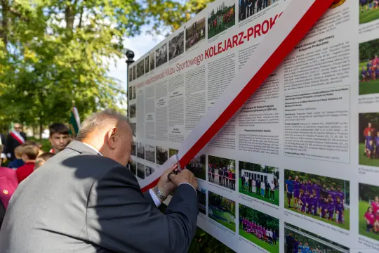 Mężczyzna podpisuje tablicę z informacjami o Klubie Sportowym Kolejarz-Prokocim.