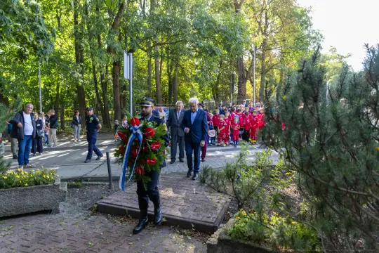 Uroczystość złożenia wieńca, uczestnicy w garniturach i czerwonych strojach.