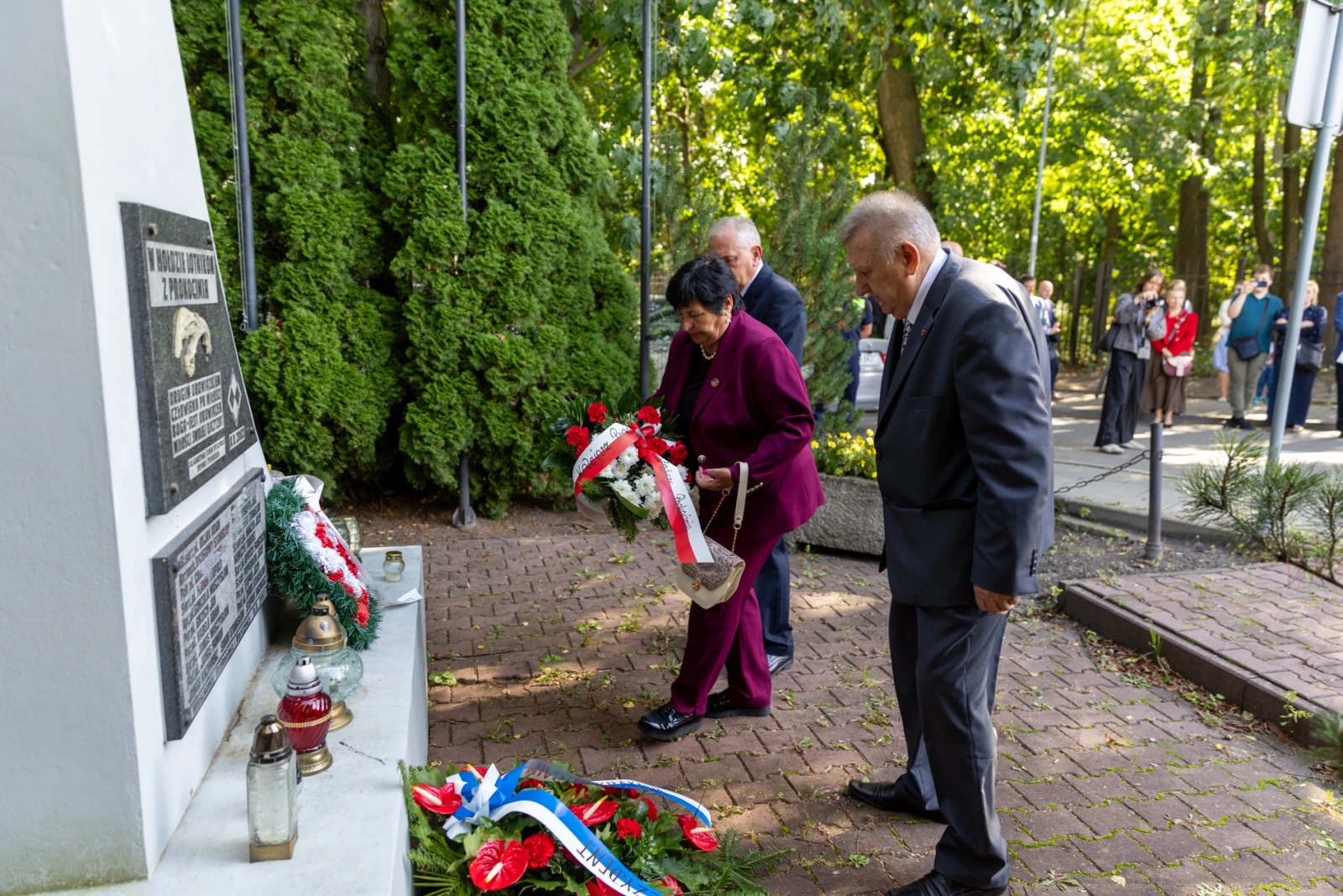 Uroczystość składania kwiatów pod pomnikiem. Obecni mężczyźni i kobieta w eleganckich strojach.  Autor: Bogusław Świerzowski