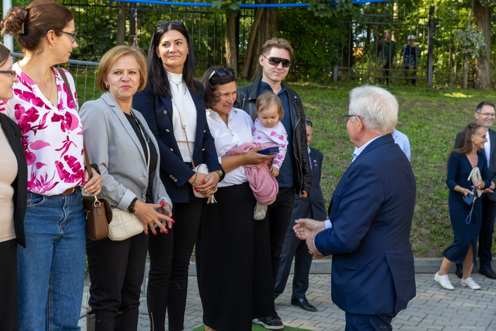 Grupa osób rozmawia w parku, jedna z kobiet trzyma dziecko na rękach.  Autor: Bogusław Świerzowski