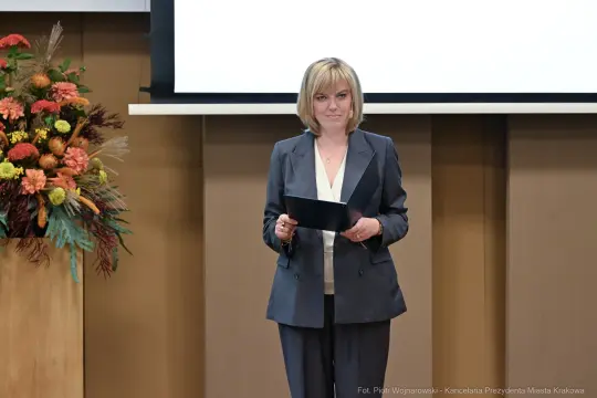 Kobieta w eleganckim garniturze trzyma tablet, stoi na tle prezentacji i dekoracji kwiatowych.