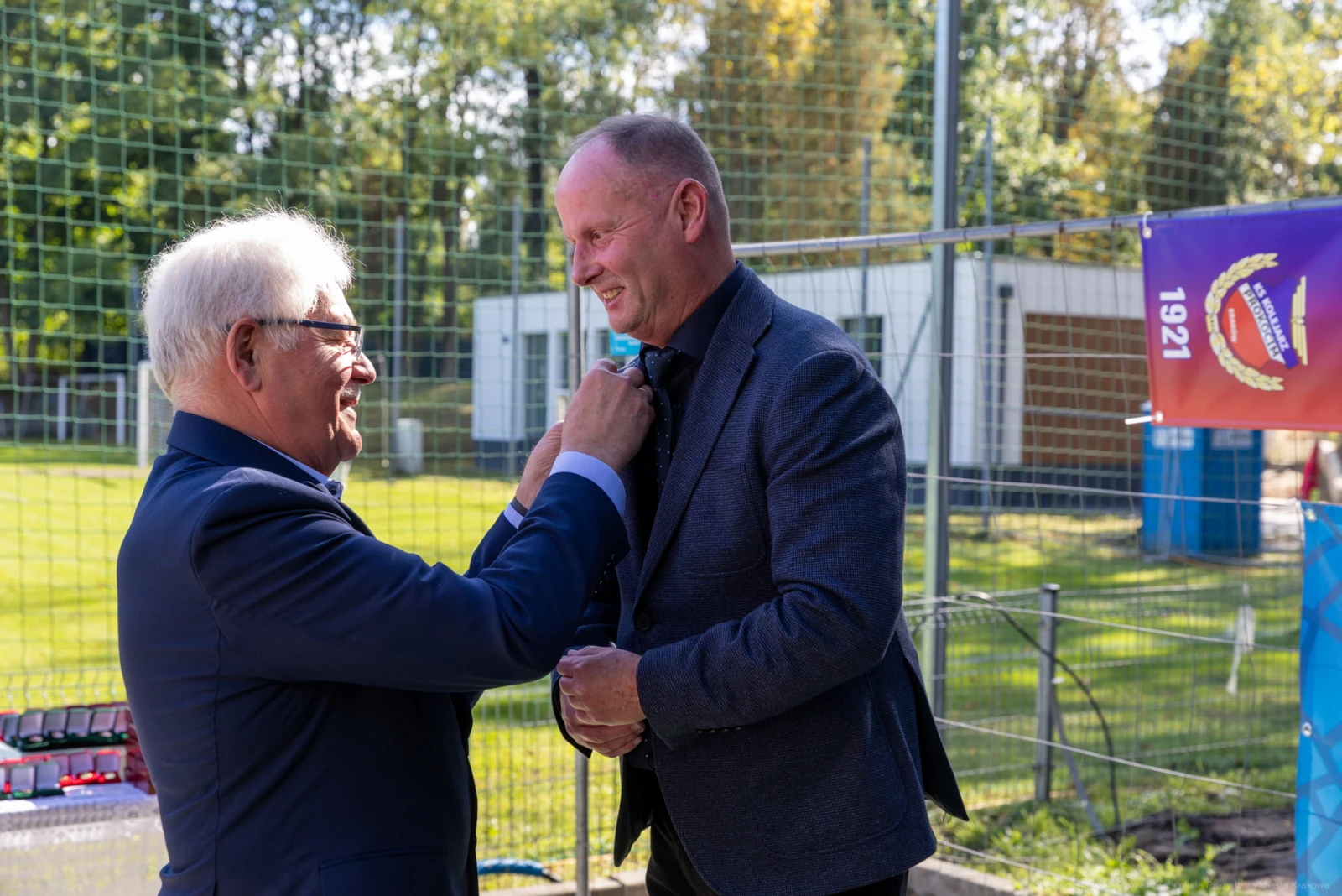 Mężczyzna przypina odznaczenie drugiemu mężczyźnie podczas uroczystości na świeżym powietrzu.  Autor: Bogusław Świerzowski