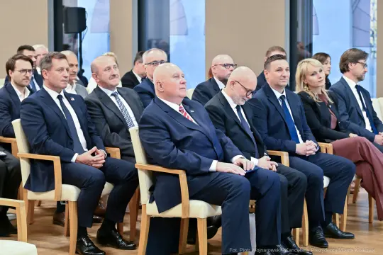 Grupa mężczyzn i kobiet w formalnych strojach siedzących w sali podczas wydarzenia.