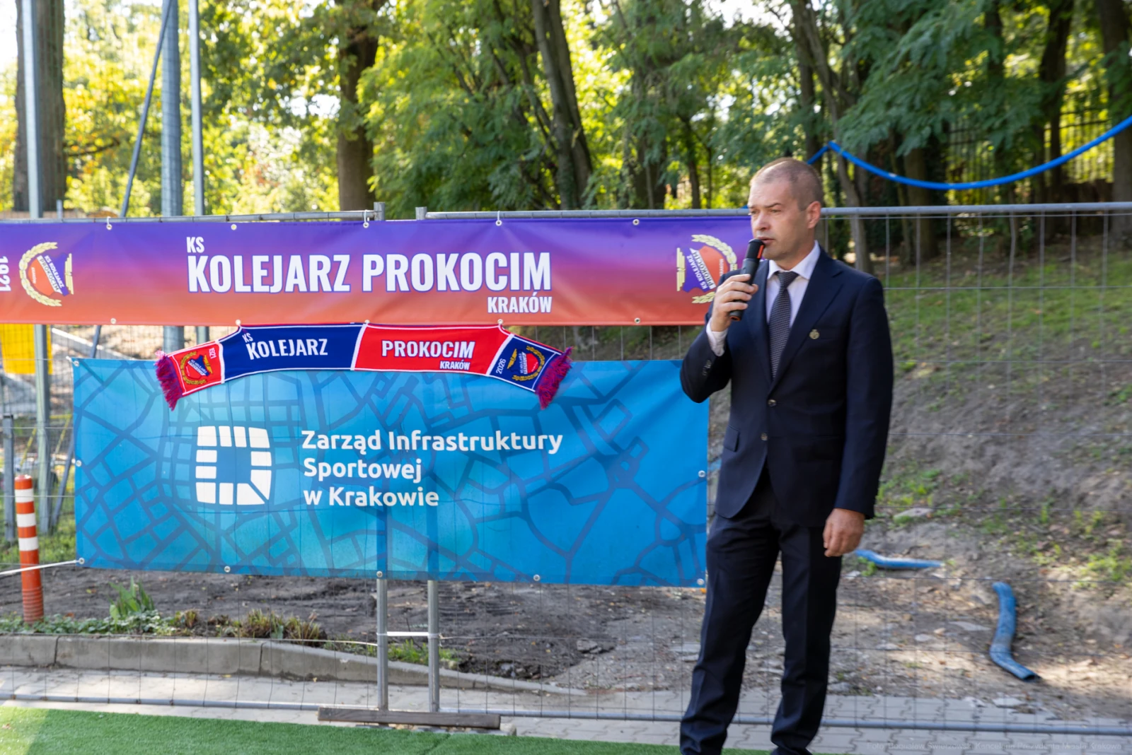 Mężczyzna w garniturze przemawia na tle bannerów związanych z klubem sportowym.  Autor: Bogusław Świerzowski