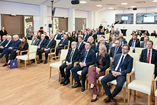 Grupa ludzi siedzących w sali podczas wydarzenia formalnego.
