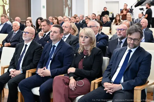 Grupa ludzi w formalnych strojach siedzących w sali podczas wydarzenia.