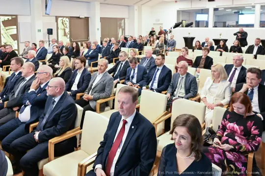 Grupa ludzi siedzących w sali podczas wydarzenia, wśród nich mężczyźni w garniturach i kobiety w eleganckich strojach.