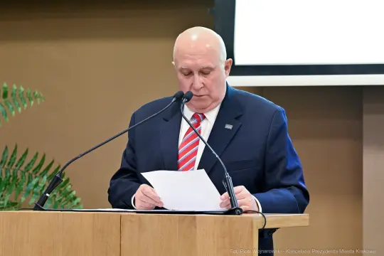Mężczyzna w garniturze przemawia z kartką w ręku przy mównicy.
