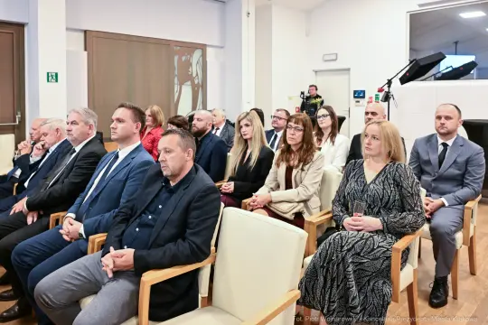 Grupa ludzi siedzących w sali, uczestniczących w wydarzeniu.