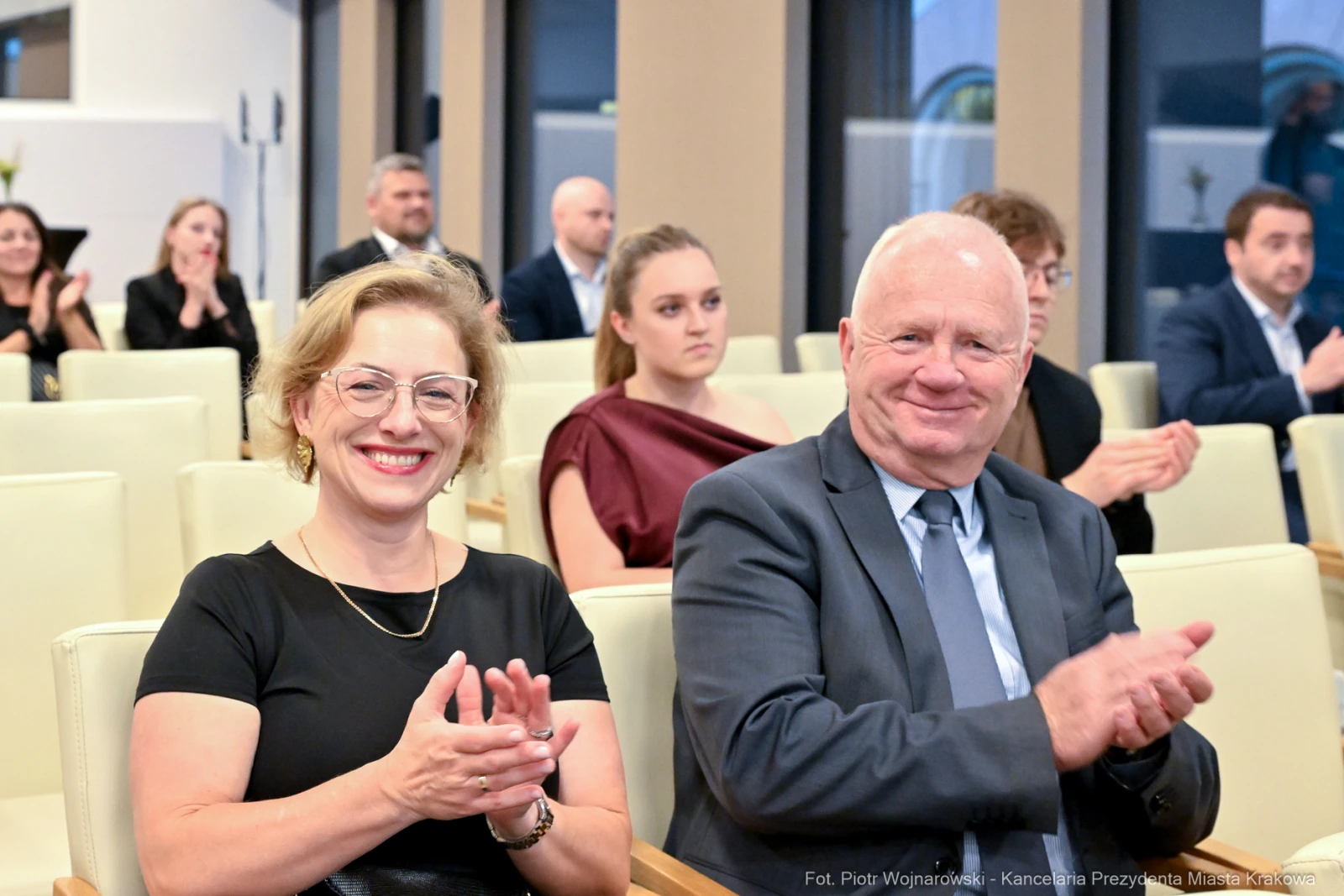 Kobieta i mężczyzna uśmiechają się i klaskają w trakcie wydarzenia. W tle widoczna grupa ludzi.  Autor: Piotr Wojnarowski