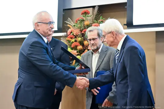 Wręczenie nagrody, uściski dłoni, kwiaty w tle.
