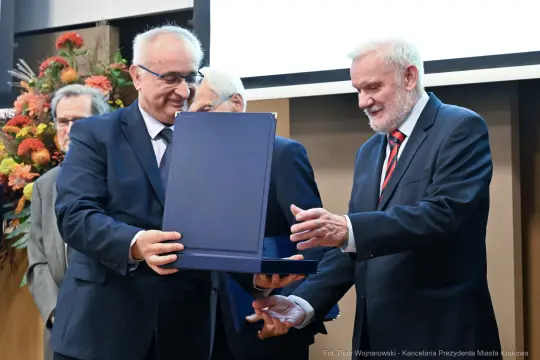 Wręczenie nagrody przez dwóch mężczyzn podczas uroczystości.