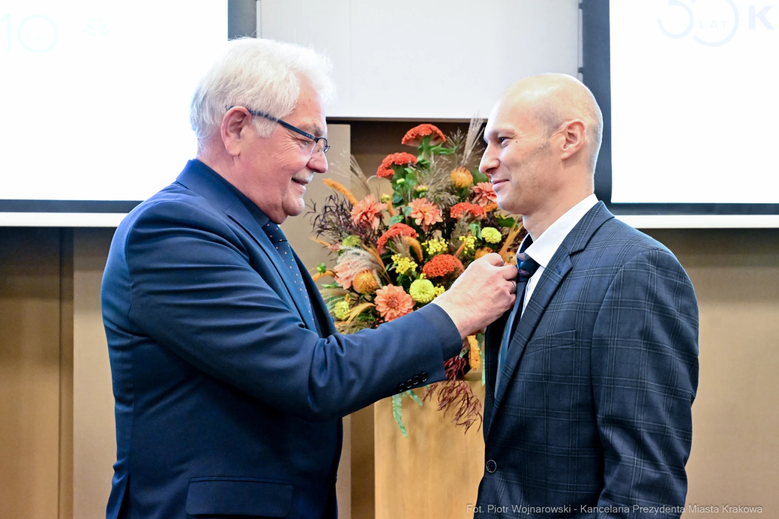 Mężczyzna w garniturze odbiera odznaczenie od innego mężczyzny w eleganckim stroju.  Autor: Piotr Wojnarowski