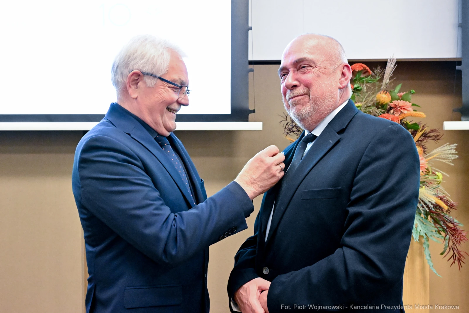 Mężczyzna przypina odznaczenie drugiemu mężczyźnie podczas uroczystości.  Autor: Piotr Wojnarowski