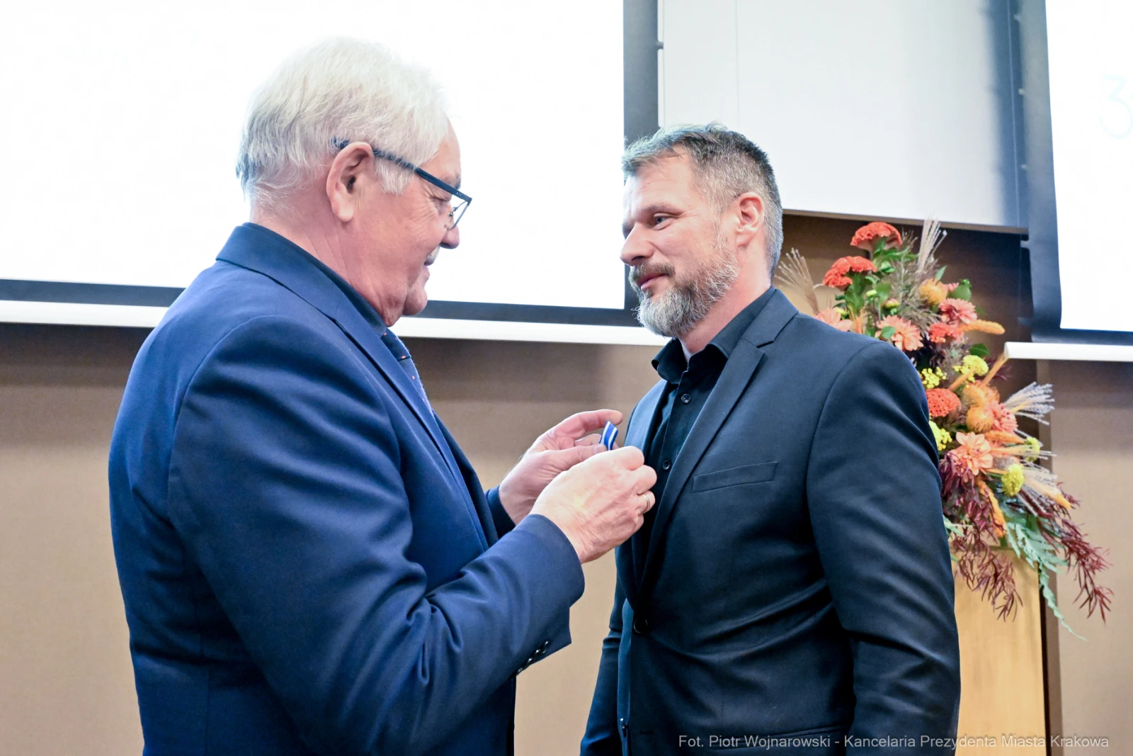Mężczyzna odbiera medal od innego mężczyzny w formalnej atmosferze.  Autor: Piotr Wojnarowski