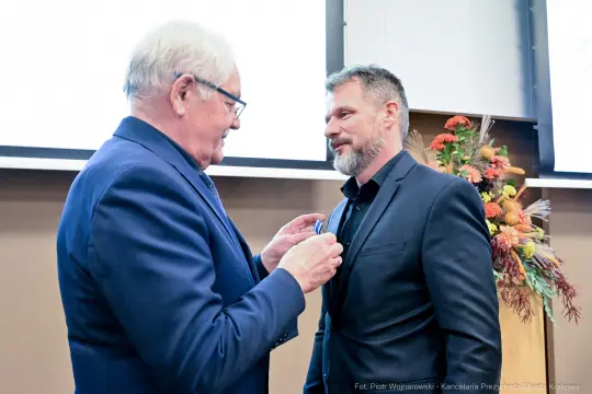 Mężczyzna odbiera medal od innego mężczyzny w formalnej atmosferze.