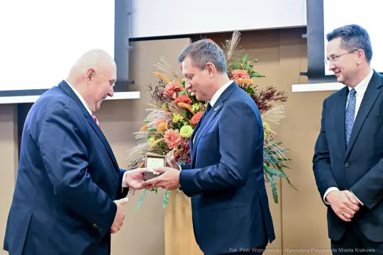 Wręczenie nagrody podczas uroczystości z kwiatową dekoracją w tle.