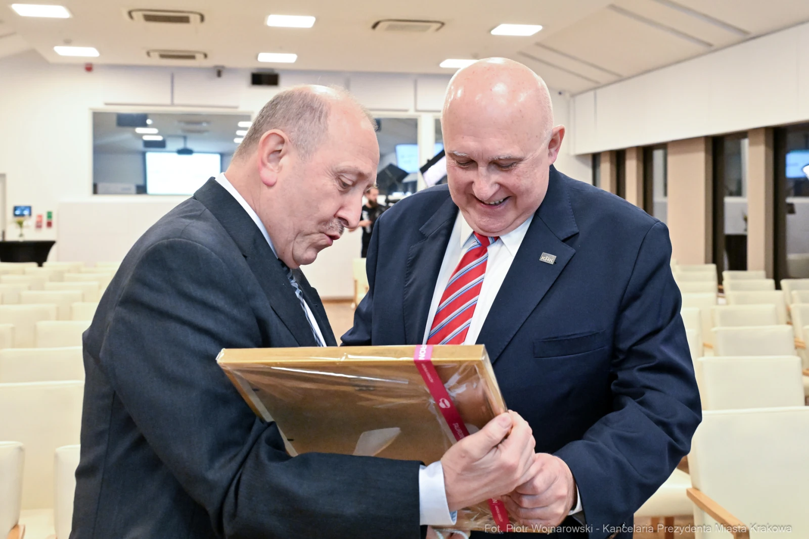 Dwaj mężczyźni uśmiechają się, trzymając ramkę z dokumentem w sali konferencyjnej.  Autor: Piotr Wojnarowski
