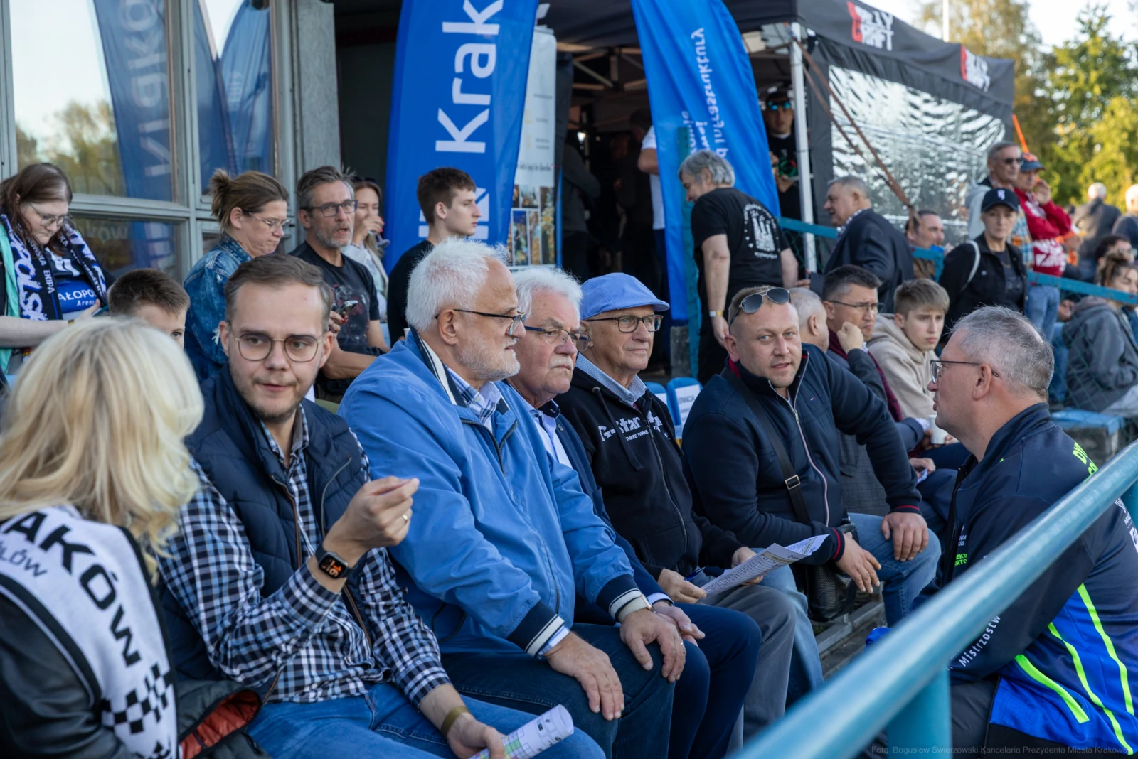 Grupa ludzi siedzących na trybunach, rozmawiających i obserwujących wydarzenie sportowe.  Autor: Bogusław Świerzowski