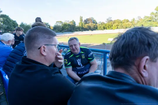 Mężczyźni w sportowych koszulkach siedzą na trybunach stadionu.