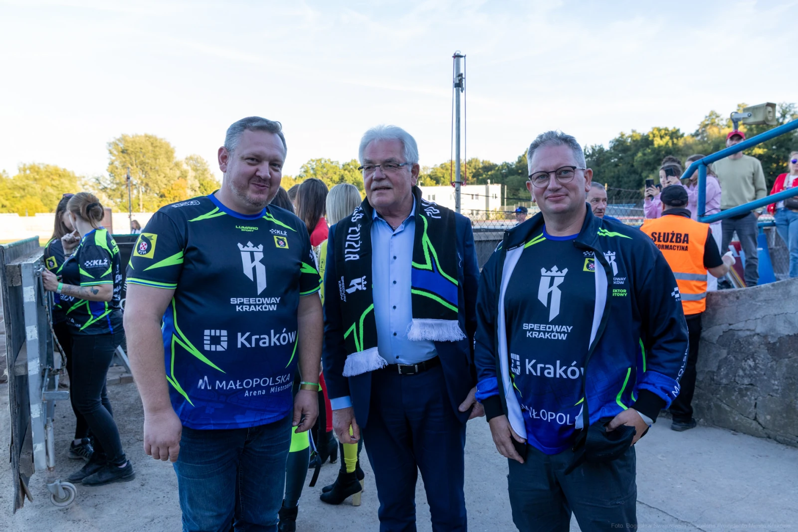 Trzech mężczyzn w strojach sportowych, z uśmiechami, na tle stadionu.  Autor: Bogusław Świerzowski