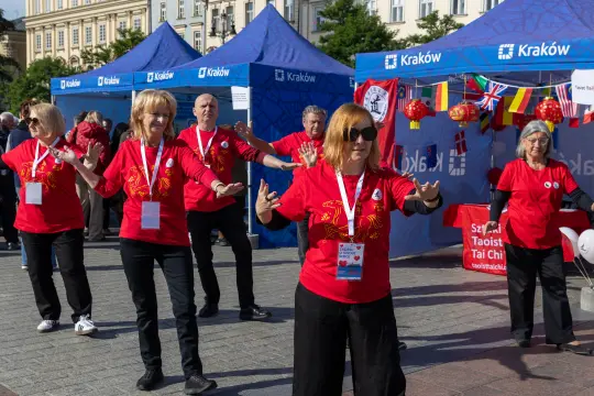 Grupa osób w czerwonych koszulkach wykonujących tai chi na tle namiotów festiwalowych.
