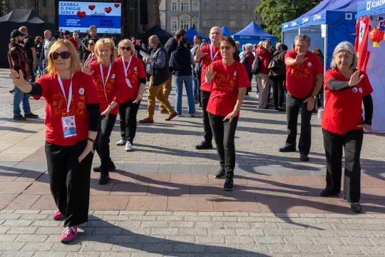 Grupa osób w czerwonych koszulkach wykonujących układ taneczny na placu.