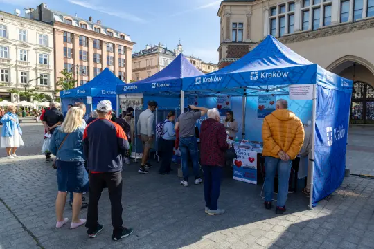 Stoiska informacyjne w Krakowie z ludźmi i materiałami promocyjnymi.