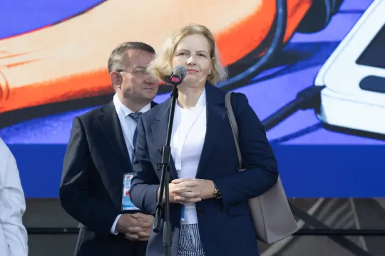Kobieta z mikrofonem na tle kolorowej grafiki, mężczyzna w tle.