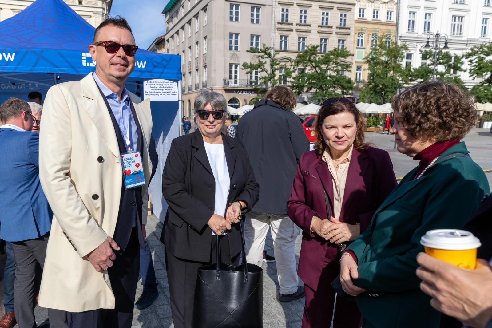 Cztery osoby rozmawiają na ulicy, w tle stoiska i budynki.  Autor: Bogusław Świerzowski