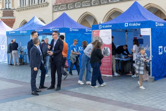 Targi z niebieskimi namiotami, ludzie rozmawiają i uczestniczą w wydarzeniu.