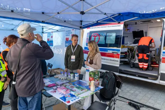 Punkt informacyjny z personelem medycznym, stołem z materiałami promocyjnymi i karetką.