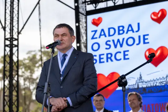 Mężczyzna w garniturze przemawia do mikrofonu, w tle hasło o dbaniu o serce.