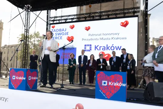 Mężczyzna przemawia na scenie podczas wydarzenia w Krakowie, w tle serca i logo miasta.