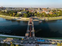 Nowoczesny most nad rzeką, z widokiem na miasto i zieleń w tle.