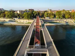 Most nad rzeką z alejkami i zielenią w tle.