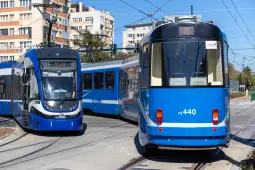 Dwa niebieskie tramwaje na skrzyżowaniu torów w miejskim otoczeniu.
