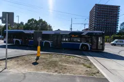Autobus skręcający na skrzyżowaniu, w tle budynek mieszkalny.