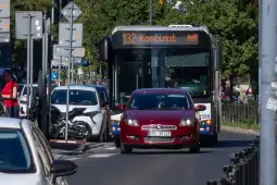 Autobus linii 132 z napisem Kombinat oraz czerwony samochód osobowy na ulicy.