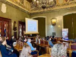Spotkanie w sali konferencyjnej z prezentacją na ekranie i uczestnikami siedzącymi w rzędach.