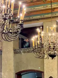 Mężczyzna grający na trąbce w eleganckim wnętrzu z żyrandolami.
