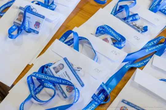 Identyfikatory z niebieskimi wstążkami leżą na białych kopertach.