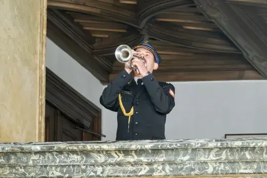 Mężczyzna w mundurze gra na trąbce z balkonu.