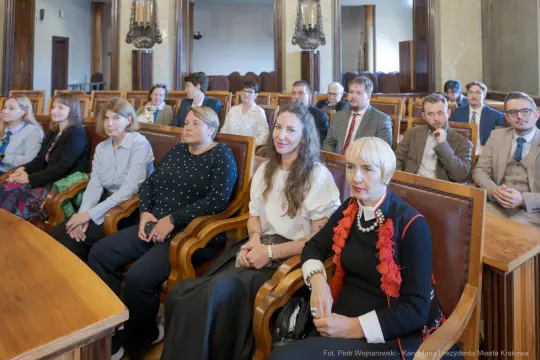 Grupa ludzi siedzących w sali obrad, w formalnych strojach, w trakcie spotkania.