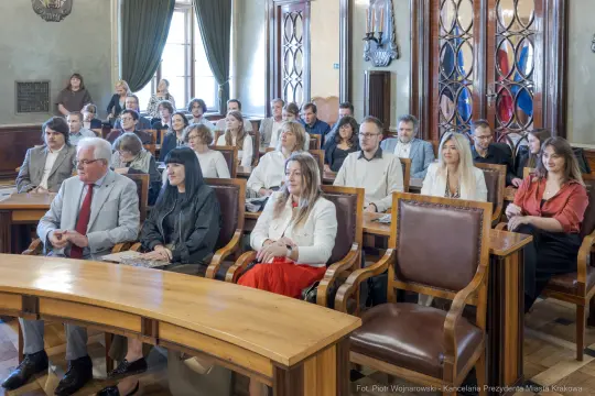 Grupa ludzi siedzących w sali, uczestniczących w wydarzeniu.